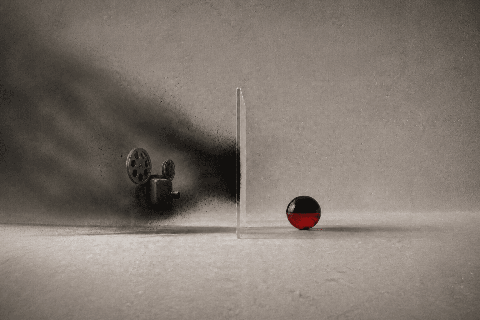 A glass barrier protects a black-and-red sphere from a cloud of dust surrounding a vintage film projector.